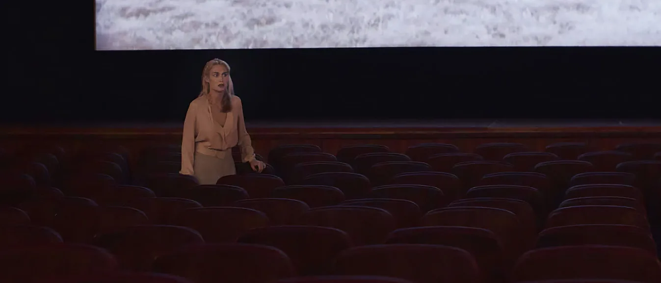 Atmospheric wide shot of actor Deborah Muriel Blum in an empty vintage cinema theater, conveying emotional depth in a dramatic scene